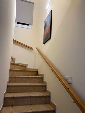 A staircase with wooden handrails and beige steps, leading to a landing with a white ceiling and a light fixture.