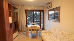 Una habitación con una mesa de comedor y sillas, un sofá, un aparador de madera y una ventana que ofrece vistas a árboles.