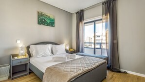 Een netjes ingerichte slaapkamer met een bed, nachtkastjes, een raam met gordijnen en een aan de muur hangend kunstwerk.