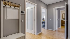 Een gang met een 'Welcome' bord, witte deuren en een zicht op een kamer met een bureau en stoel.