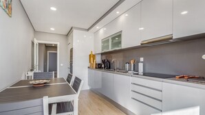 Een moderne keuken met een eethoek, met een houten tafel en stoelen, een inbouwoven en een roestvrijstalen spoelbak.