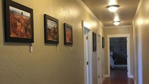 A hallway with framed pictures on the walls, a wooden floor, and doors leading to other rooms. - Bryce Canyon, Zion National Park A Six K (Panguitch)