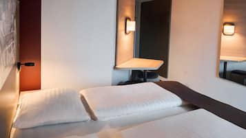 Quarto de hotel com cama, uma mesa pequena, espelho e luminária na parede.