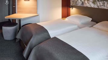 Habitación de hotel con dos camas, una mesita y una lámpara fijada a la pared.
