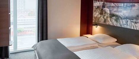 Une chambre d’hôtel avec un grand lit, une fenêtre avec des rideaux et une œuvre d’art accrochée au mur.