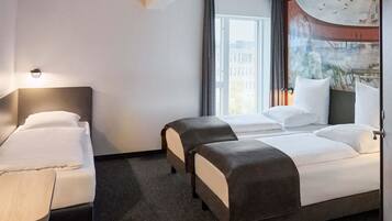 A hotel room with two beds, a desk, and a large window with a view of buildings and birds.