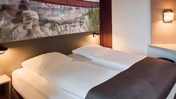 A hotel room with a bed, a nightstand, a wall-mounted light, and a painting above the bed.