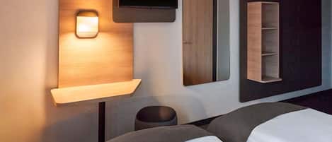 Habitación de hotel con dos camas, un televisor montado en un panel de madera, un espejo y una repisa con luz.
