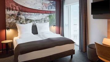 A hotel room with a large bed, a small table, a chair, a TV, and a window with curtains.