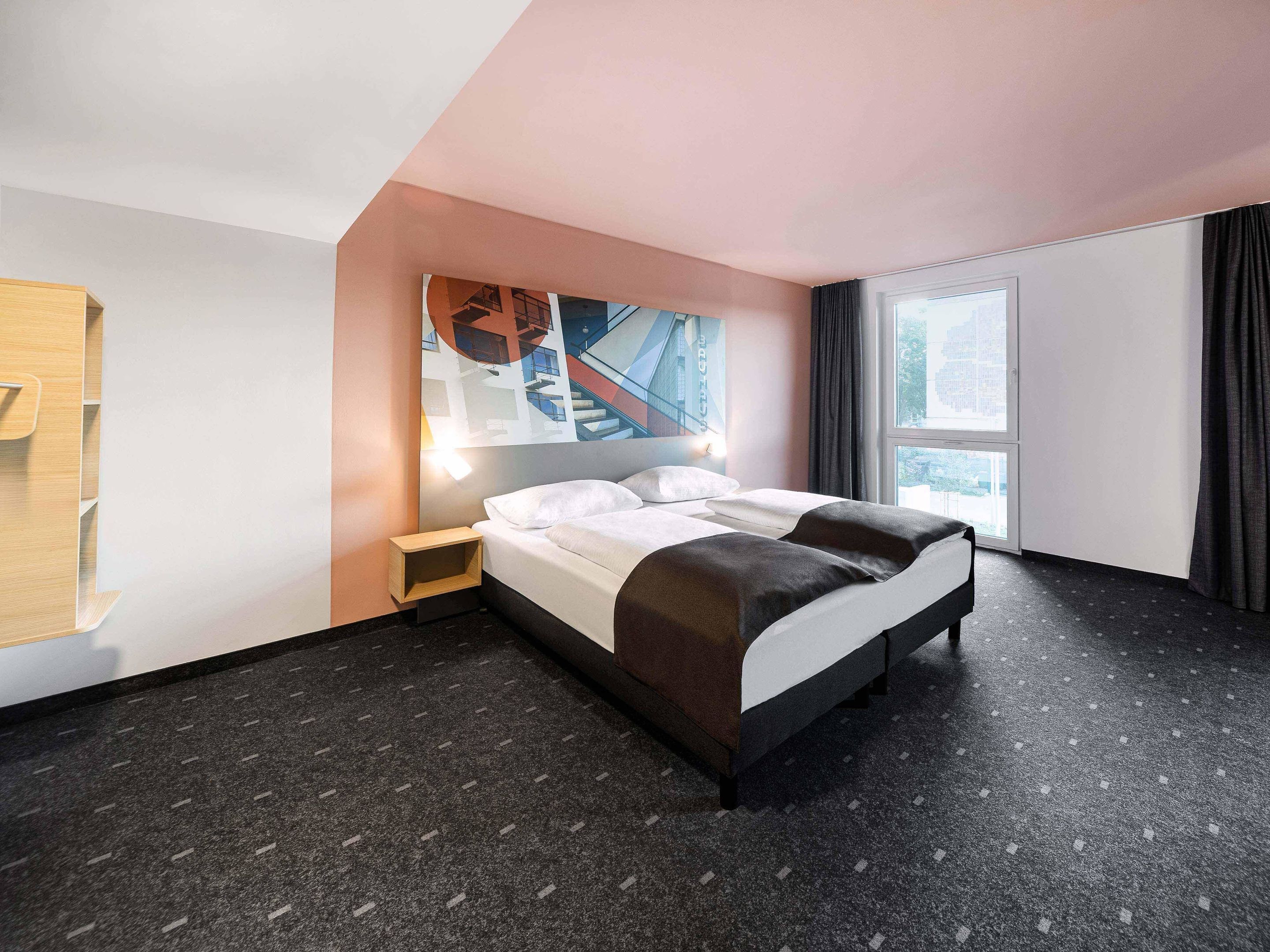 Une chambre d’hôtel moderne avec un grand lit, une table de chevet, un téléviseur fixé au mur et une fenêtre avec des rideaux.
