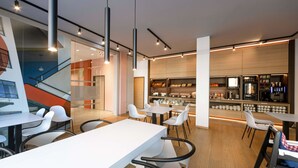 Een modern café met witte tafels en stoelen, een bar met een counter en planken, en een trap op de achtergrond.
