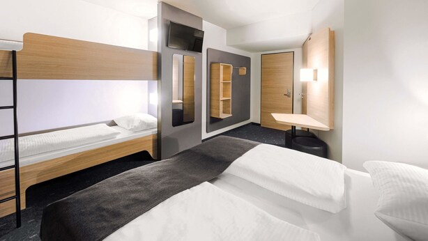 Ein Hotelzimmer mit Etagenbett, Nachttisch, Spiegel und kleinem Schreibtisch mit Stuhl.