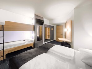Une chambre d’hôtel avec un lit superposé, une table de chevet, un miroir et un petit bureau avec une chaise.