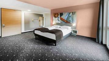 A modern hotel room with a large bed, a small bedside table, a built-in shelf, and a painting on the wall.
