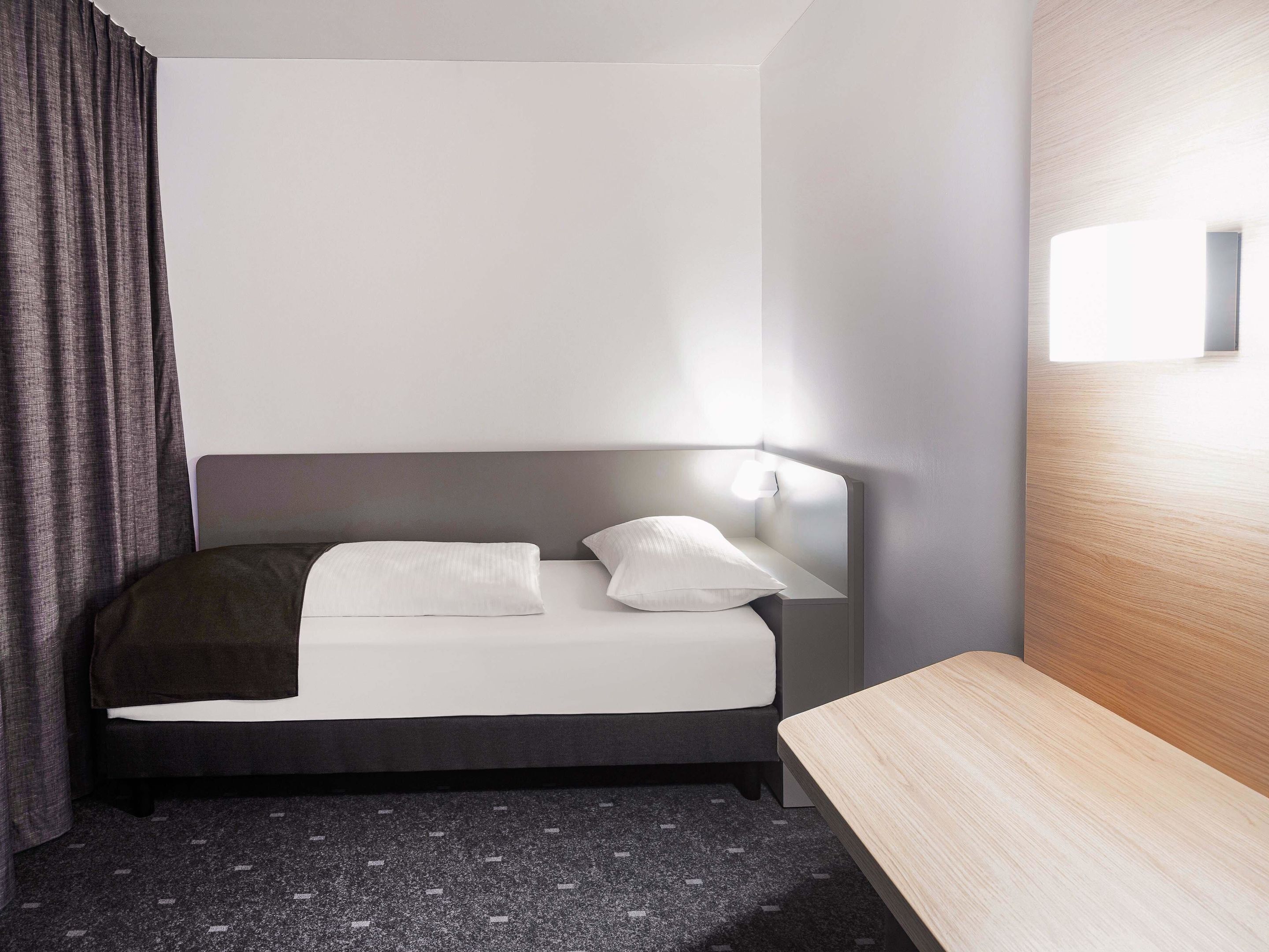 Ett modernt hotellrum med en säng, ett sängbord och en sänggavel med en lampa.