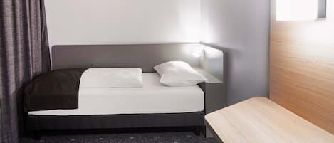 A modern hotel room with a bed, a bedside table, and a headboard with a light fixture.