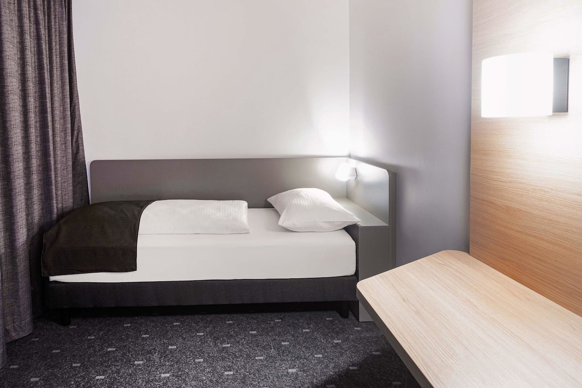 Una habitación de hotel moderna con cama, mesita de noche y cabecero con lámpara.
