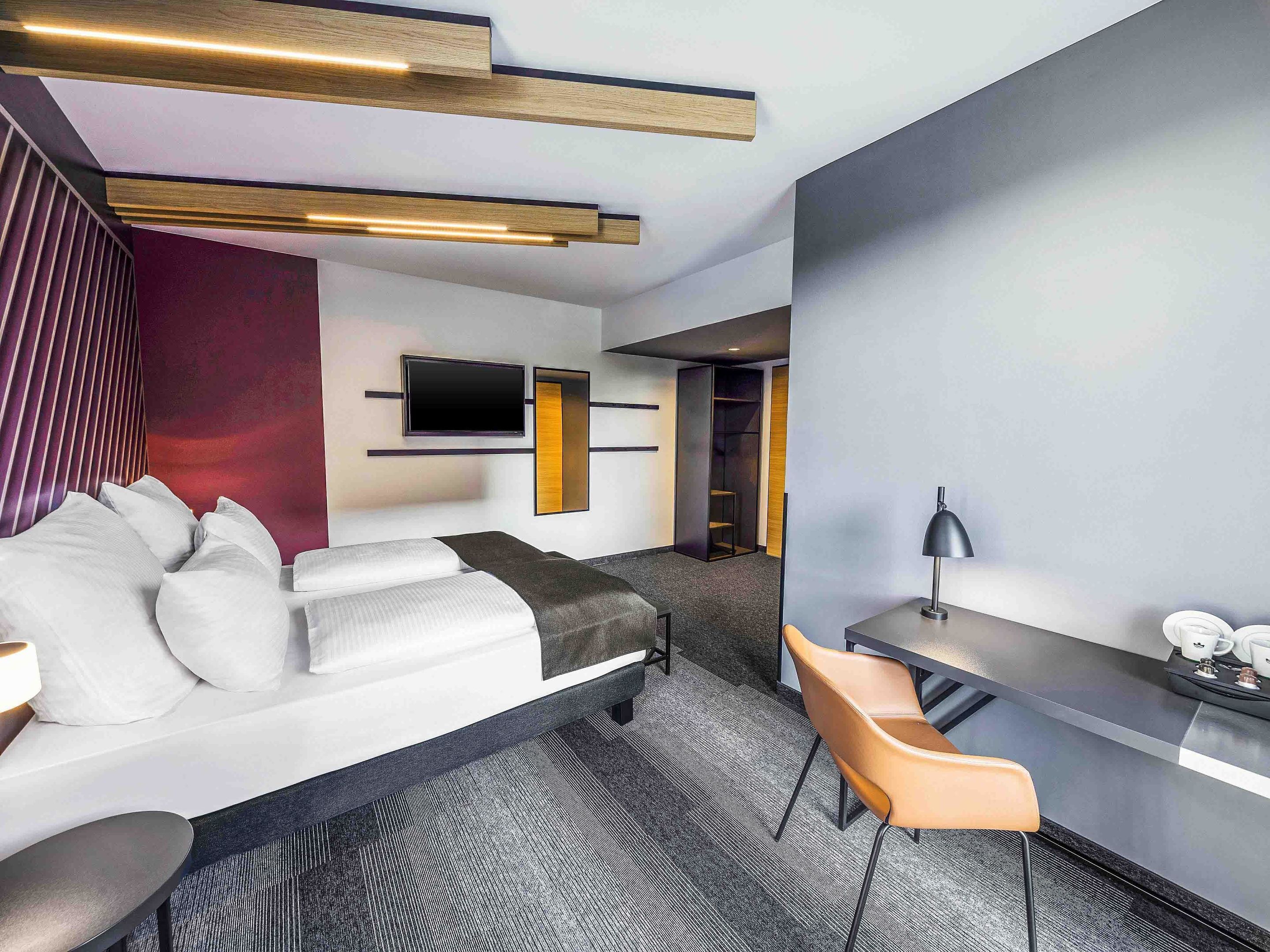 Ett modernt hotellrum med en soffa, ett skrivbord, en stol, en platt-TV och en bokhylla.
