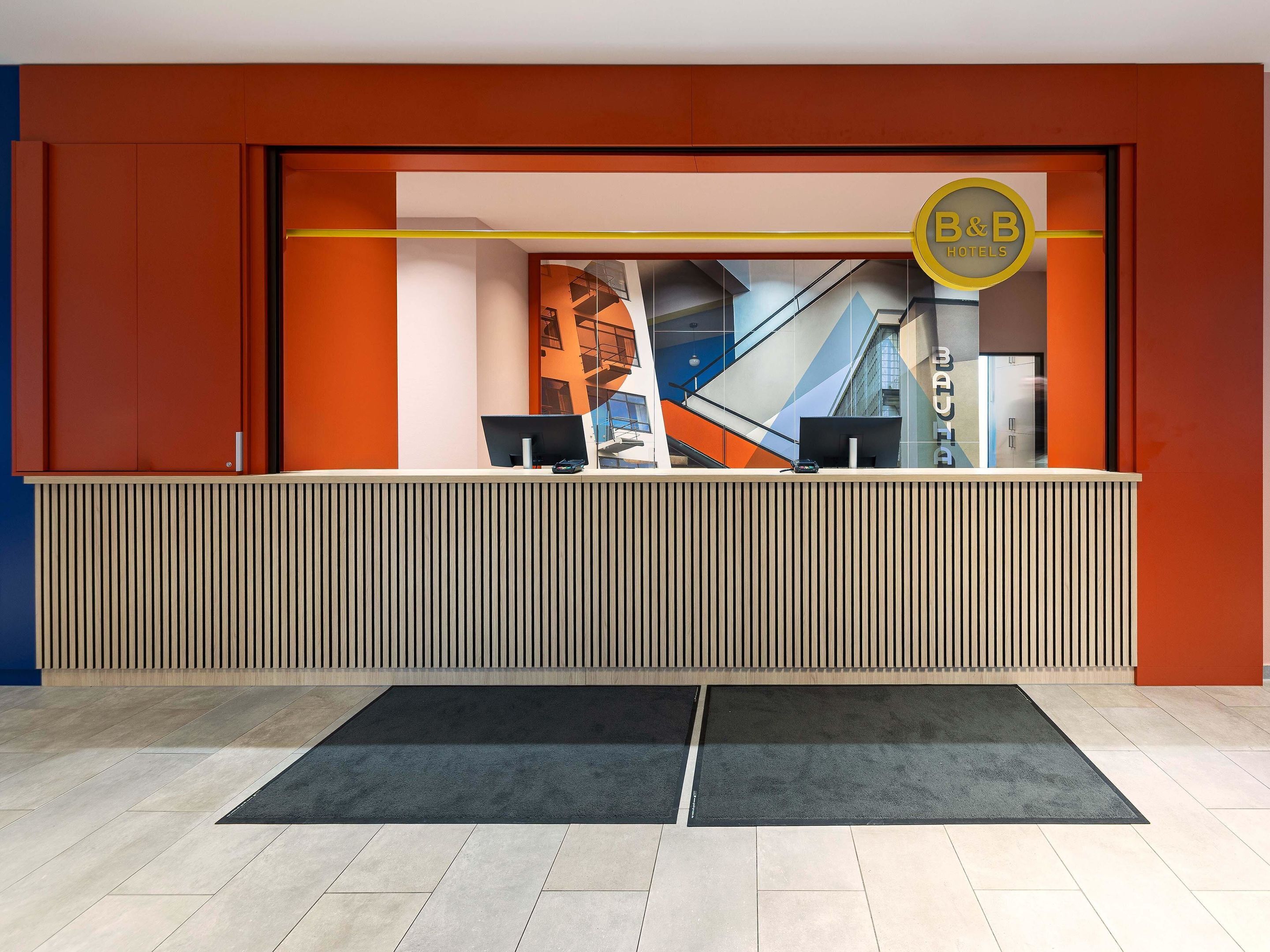 Een modern ontworpen hotel receptiebalie, met een logo en een glazen scheidingswand.
