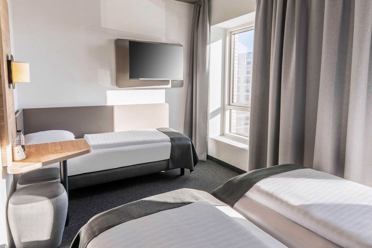 Une chambre d’hôtel avec un lit, un bureau, une télévision et une fenêtre avec des rideaux.