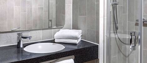Une salle de bain moderne avec un plan de toilette en granit noir, un lavabo blanc et une douche à parois de verre.