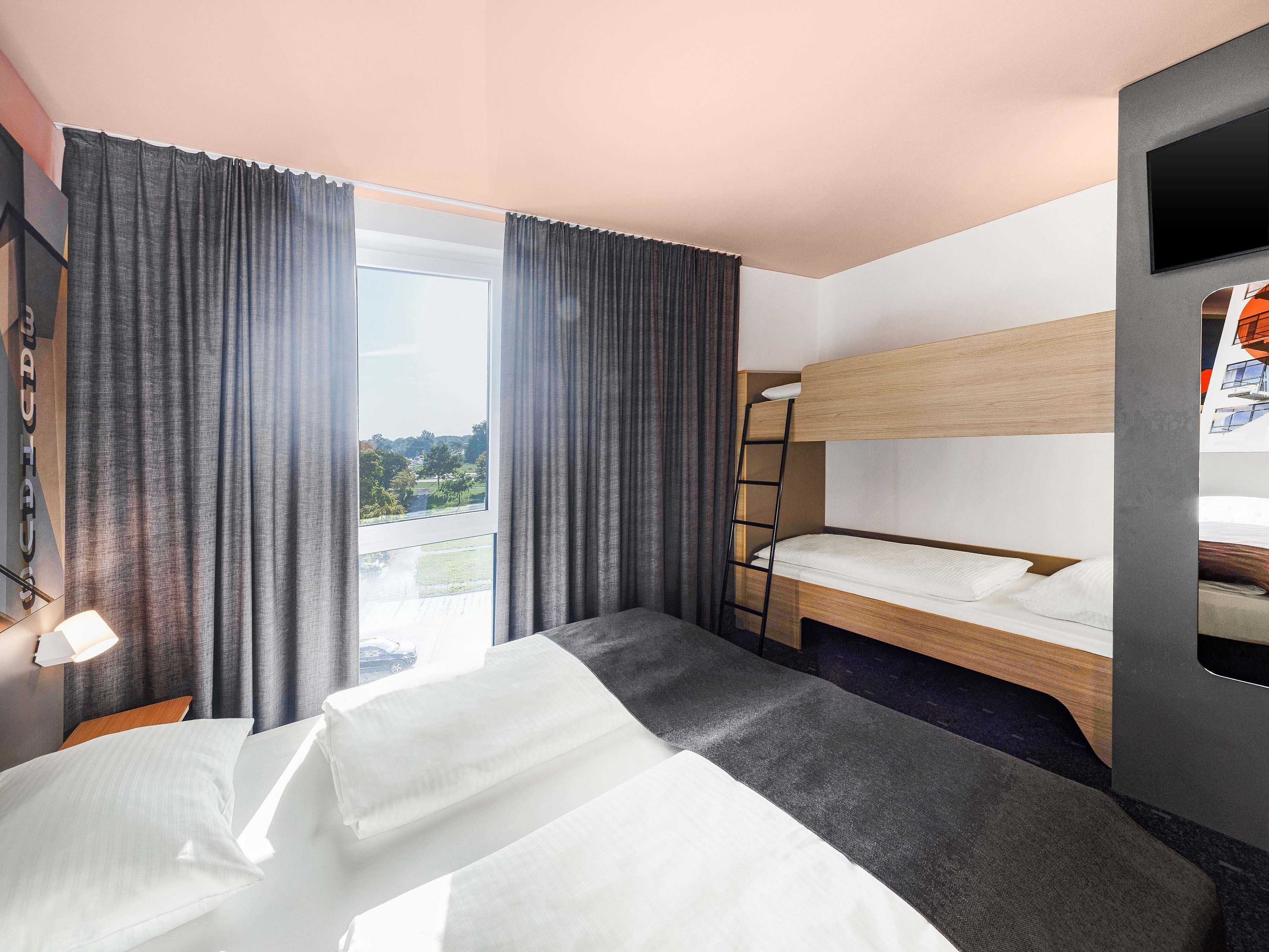 Una habitación de hotel con una cama litera, un escritorio, una silla y un ventanal con cortinas.