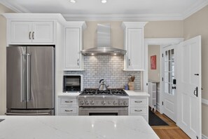 Una cocina moderna con armarios blancos, electrodomésticos de acero inoxidable, estufa a gas y horno empotrado.