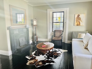 Una habitación con chimenea, un reloj, una silla, un sofá y un tapiz de cuero de vaca.
