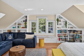 Un dormitorio tipo loft con un sofá azul oscuro, una mesita auxiliar amarilla, una cama blanca y una estantería llena de libros y juguetes.