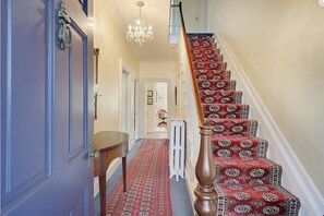 A staircase with a red patterned carpet, a wooden handrail, and a chandelier.