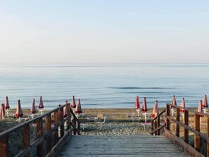 Pasarela de madera que conduce a sillas de playa y sombrillas.