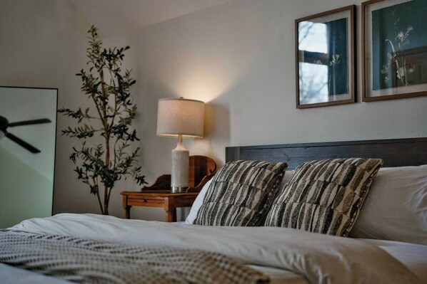 A neatly made bed with striped pillows, a bedside lamp, a nightstand, and a wall-mounted clock.