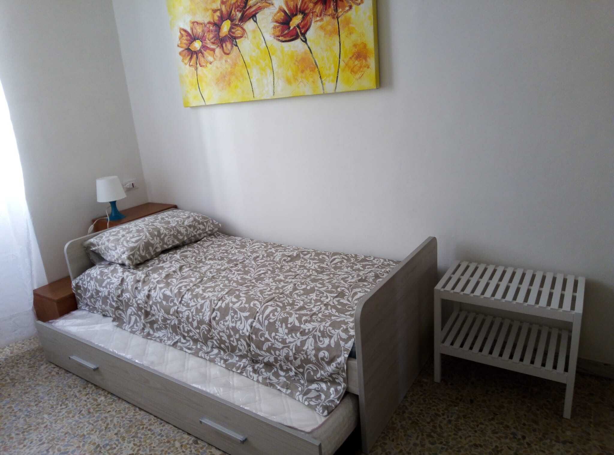A small, neatly arranged bedroom with a single bed, a bedside table with a lamp, and a radiator.