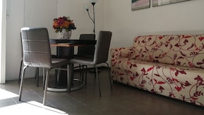 Un comedor con una mesa, sillas, un jarrón de flores, un sofá y dos cuadros en la pared.