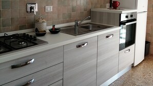 Una cocina moderna con estufa a gas, pileta de acero inoxidable y alacenas blancas.