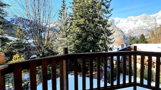 A wooden deck with a view of snow-covered mountains and a traditional chalet. - Mont Blanc Apt- Bluchalet  (Courmayeur)