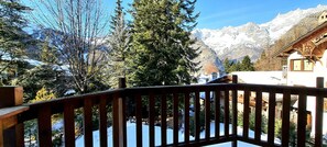 Um deck de madeira com vista para montanhas cobertas de neve e um chalé tradicional.
