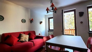 A room with a red sofa, a dining table, and chairs. There are decorative plates on the wall and a chandelier. - Mont Blanc Apt- Bluchalet  (Courmayeur)
