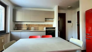 A compact kitchen with a white table, red chairs, a red refrigerator, and a window. - Mont Blanc Apt- Bluchalet  (Courmayeur)