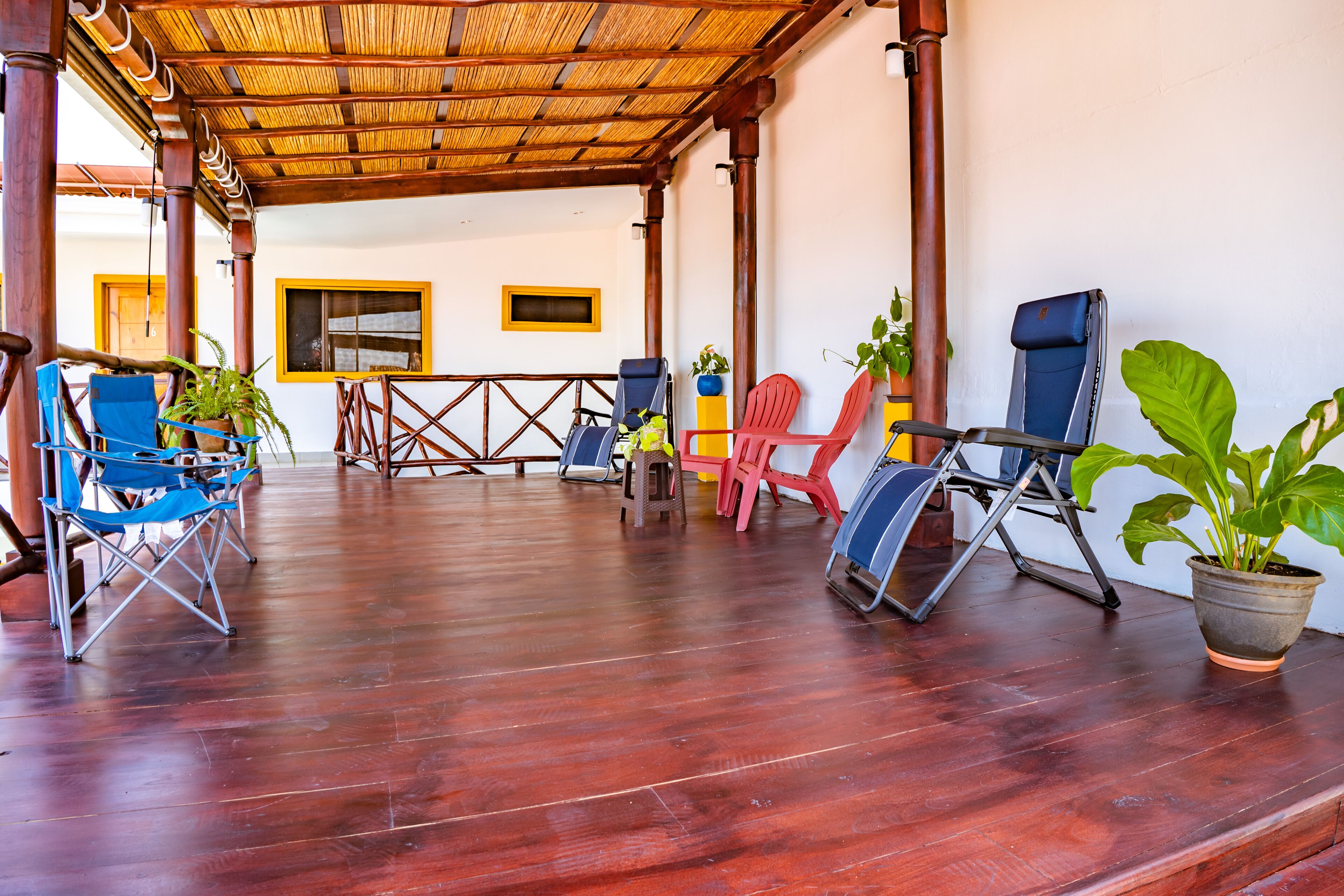 An open-air covered patio with wooden flooring, several folding chairs, and potted plants.
