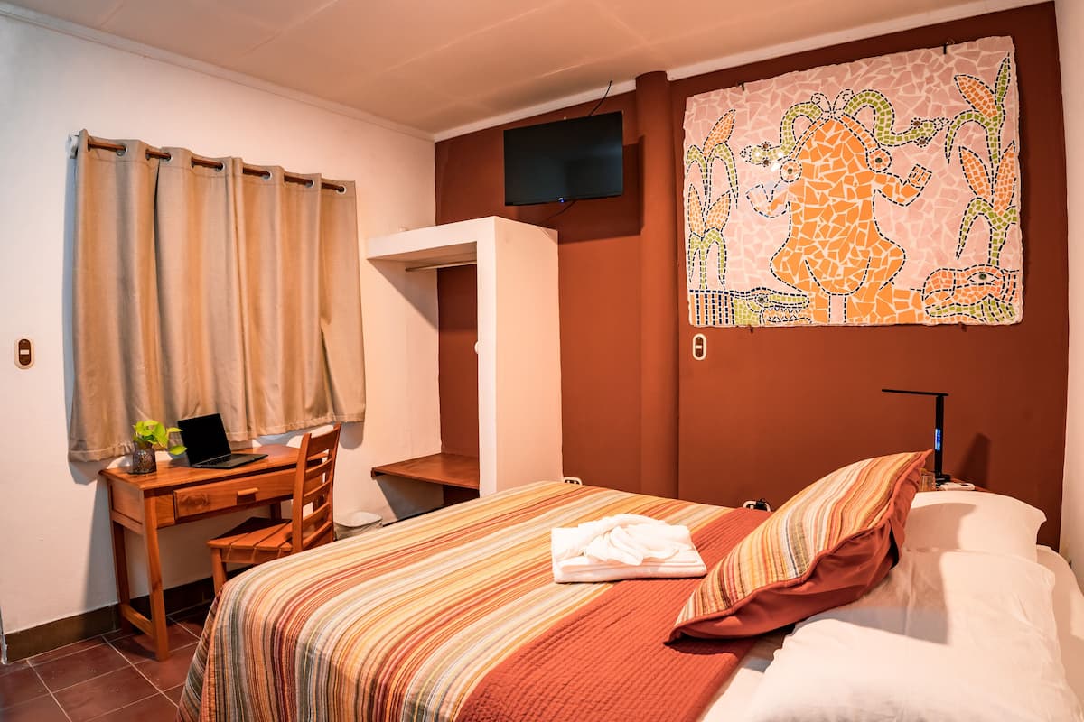 Une chambre d’hôtel avec un lit, un bureau avec un ordinateur portable, une télévision et une œuvre d’art murale.