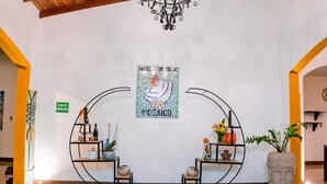 Een hal met een houten plafond, vloertegels met een patroon, een kroonluchter en een mozaïek kunstwerk aan de muur.
