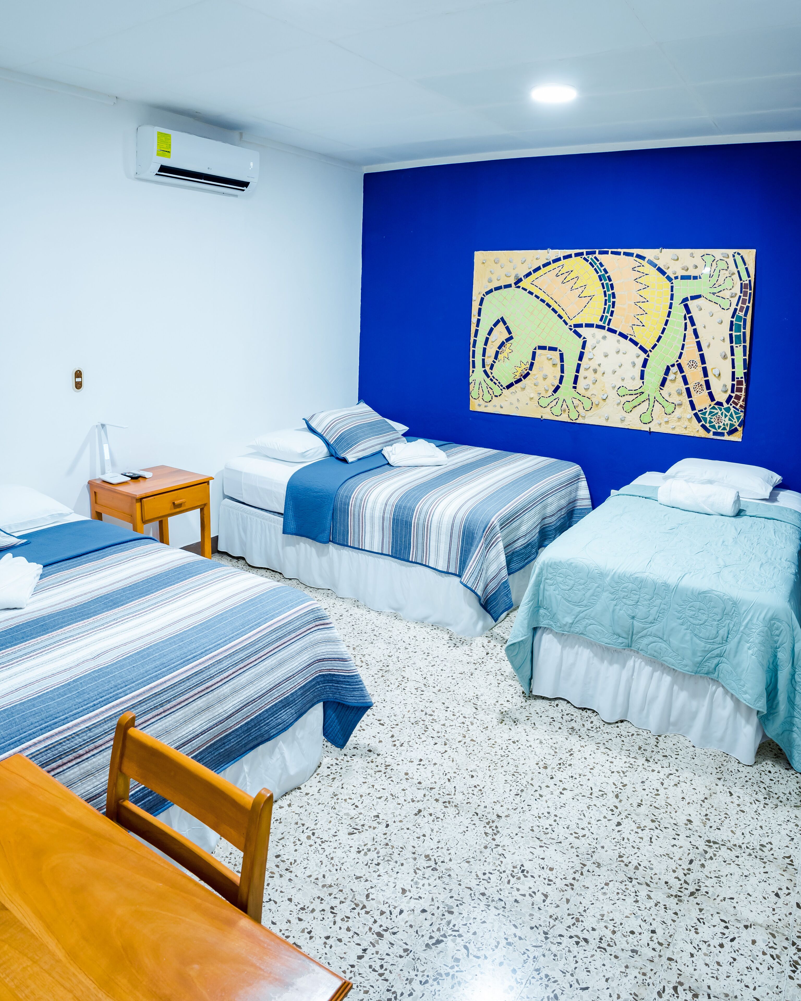 A hotel room with two beds, a wooden table, a small bedside table, and a wall-mounted air conditioner.