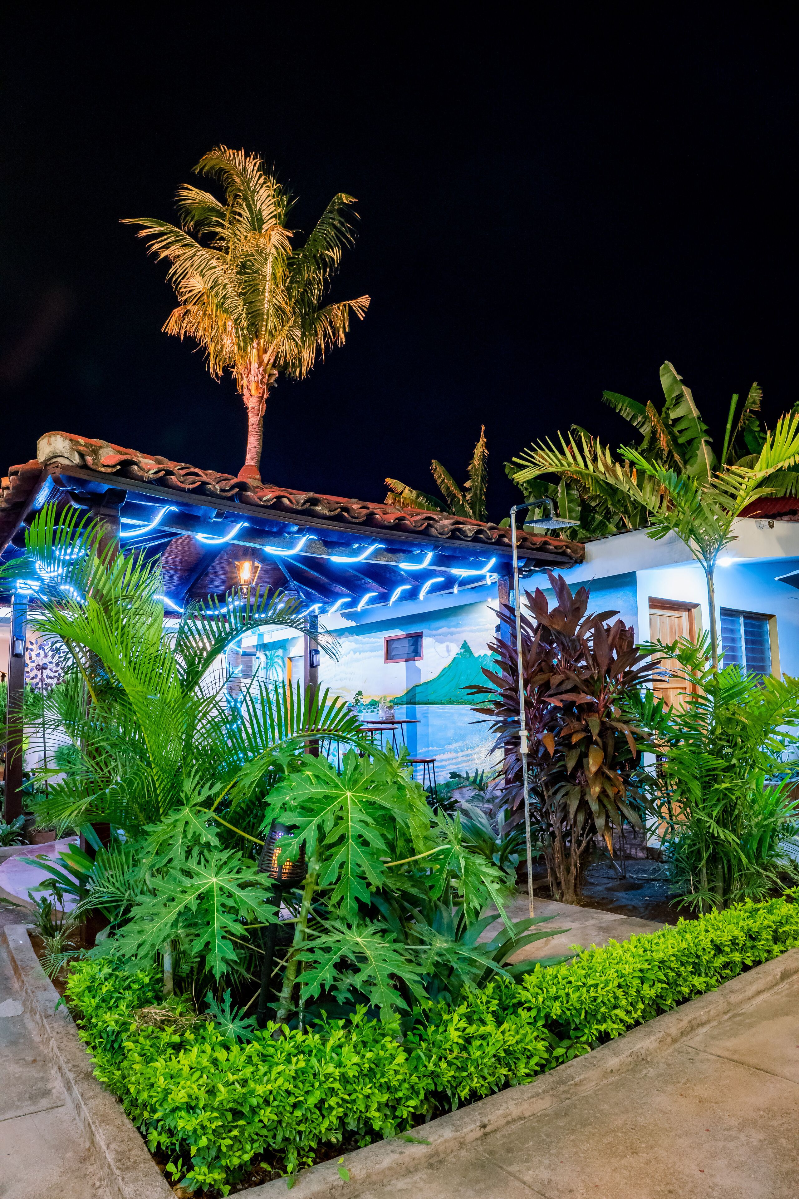 A building with a tiled roof, surrounded by lush greenery including palm trees and various plants.