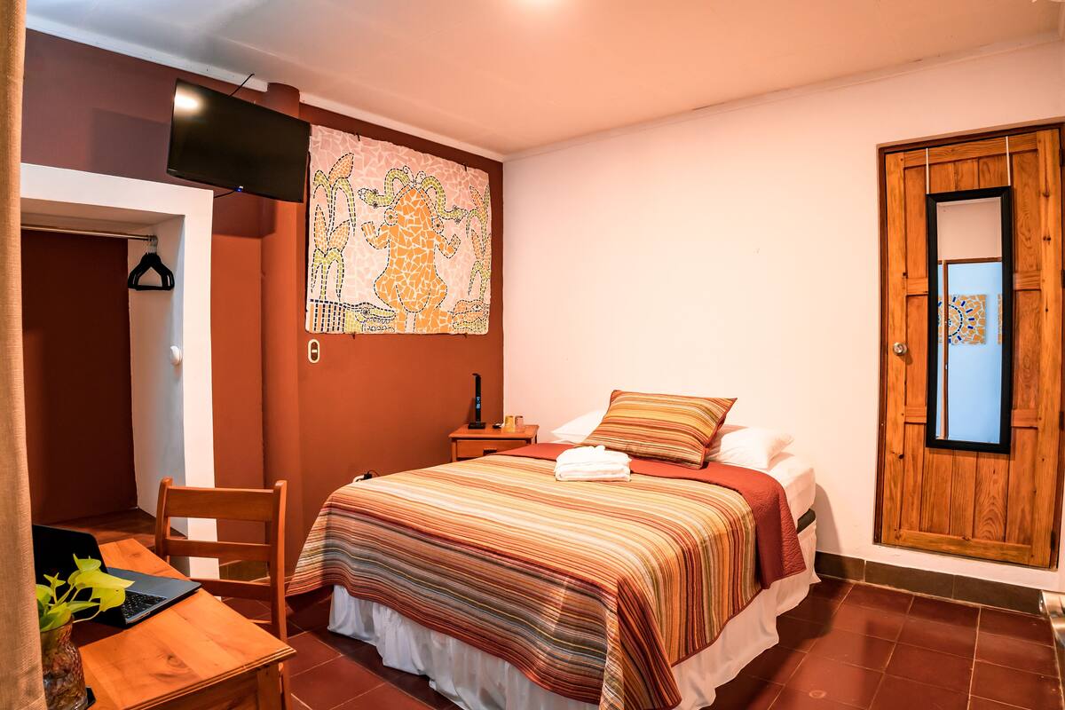 Une chambre à coucher avec un lit, un bureau avec un ordinateur portable, une chaise, une télévision et une porte en bois.