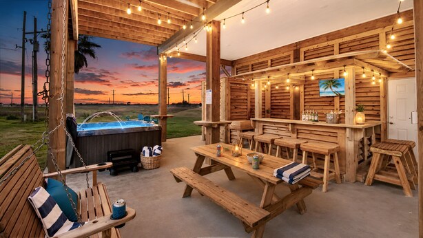 Eine hölzerne Terrasse im Freien mit Whirlpool, Holzbanken, Picknicktischen, Lichterketten und Blick auf den Sonnenuntergang.