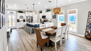 Une cuisine moderne avec des meubles blancs, un îlot central et un coin repas avec des chaises blanches.