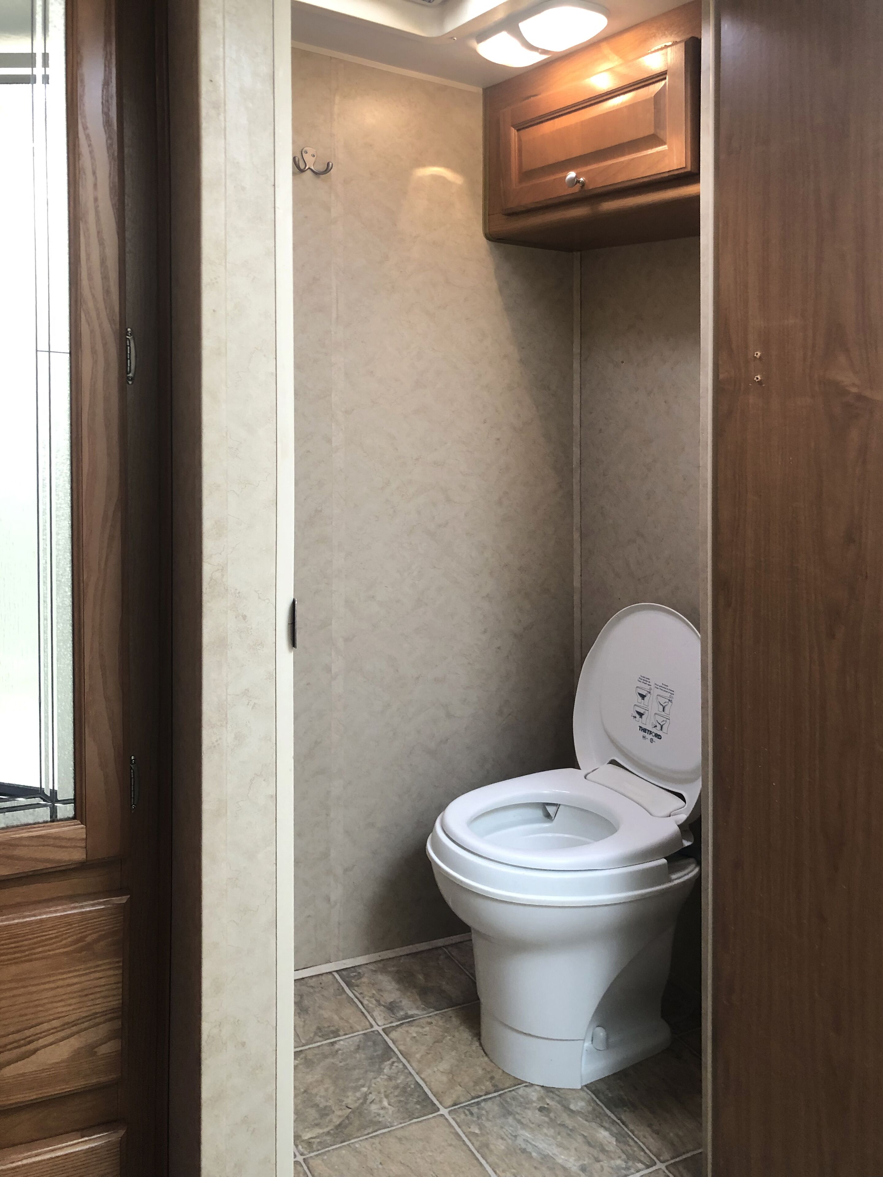 A bathroom with a white toilet, wooden cabinetry, and a tiled floor.