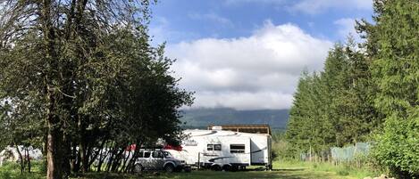 Een witte camper staat op een grasveld, met bomen en bergen op de achtergrond.