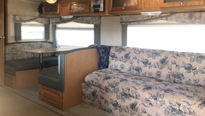 A compact RV interior with a kitchenette, a dining table, and a sofa. - Misty Haven Farm (Ladysmith)